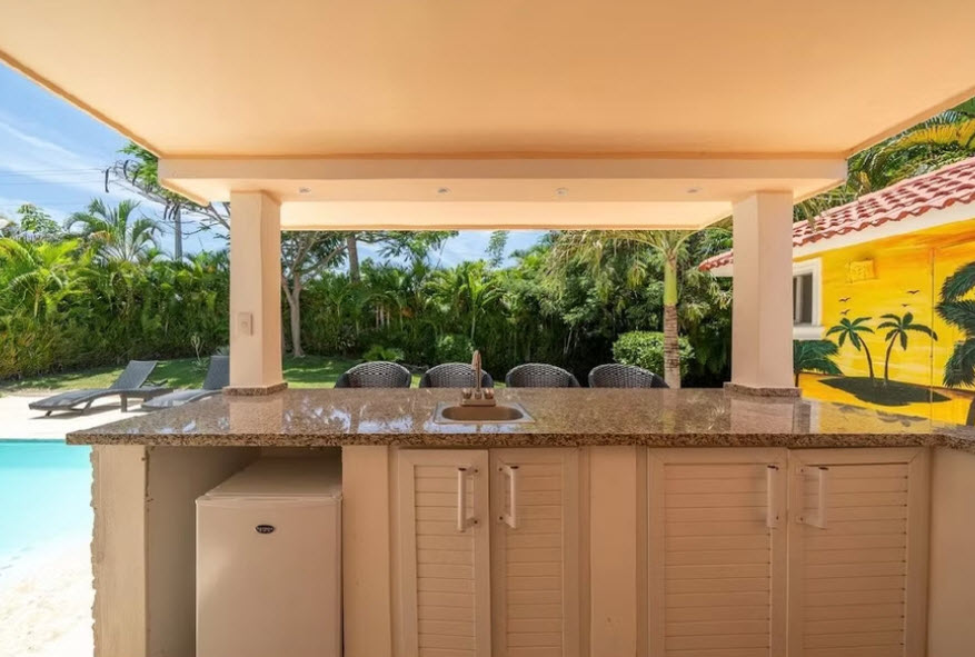 Outdoor bar with sink, mini-fridge, and tropical mural by a pool