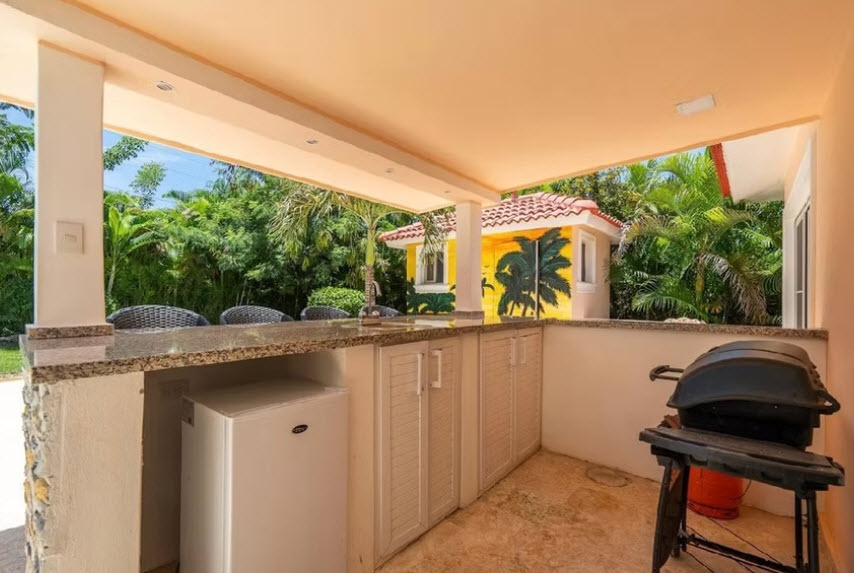 Outdoor kitchen with grill, mini fridge, and tropical foliage