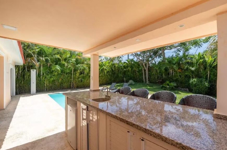Outdoor kitchen bar with granite countertop overlooking a tropical pool and garden