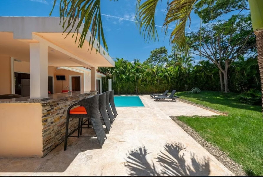 Tropical villa with outdoor bar, pool, and lounge chairs under palm trees