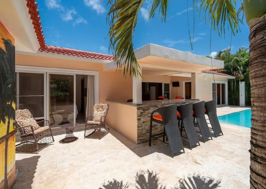 Tropical villa patio with pool, bar, and seating under palm trees