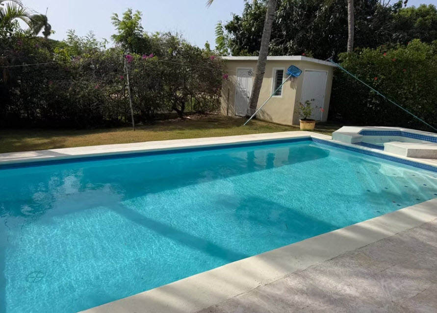 Crystal clear swimming pool with lounge area in a lush backyard oasis.