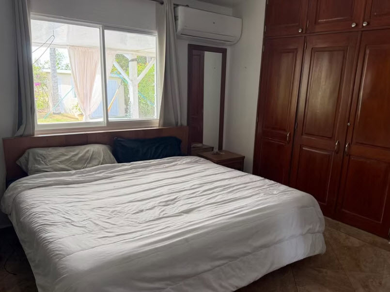 Bedroom with large white bed, wooden wardrobe, and window view