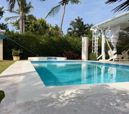 Tropical villa with a sparkling blue swimming pool surrounded by lush green palm trees.