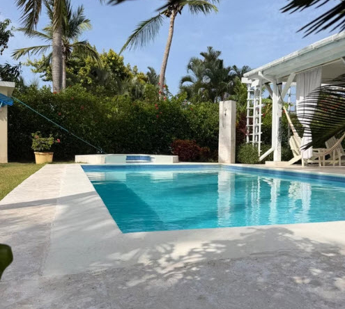Tropical villa with a sparkling blue swimming pool surrounded by lush green palm trees.