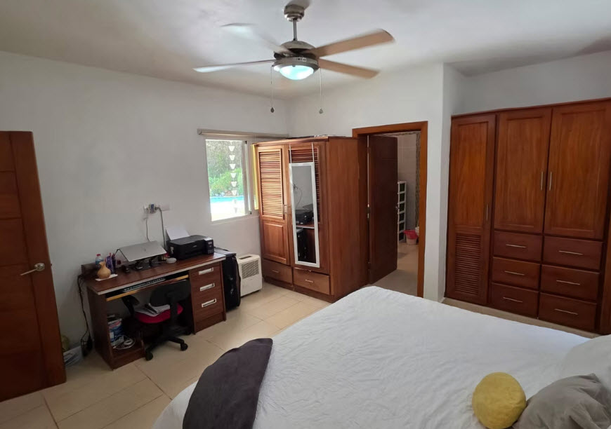 Spacious bedroom with a desk, wardrobe, and view of a pool through the window