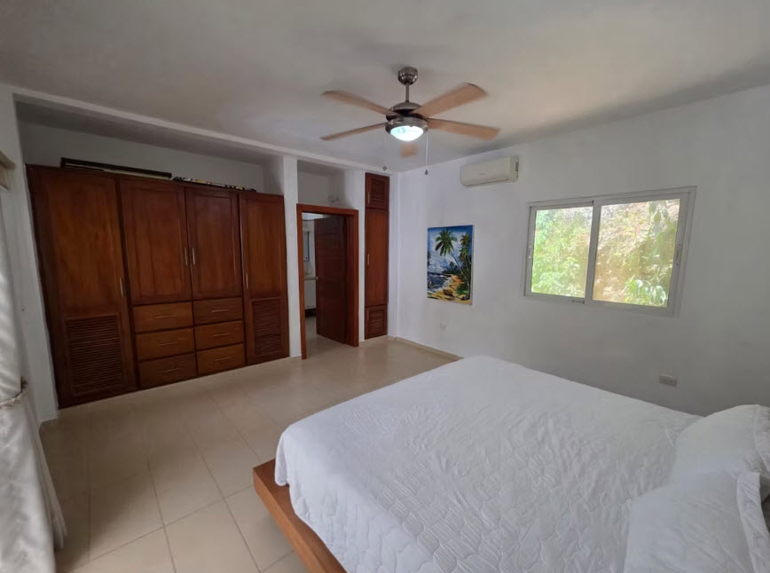 Spacious bedroom with large wooden wardrobes, a king-size bed, and a window overlooking lush greenery.