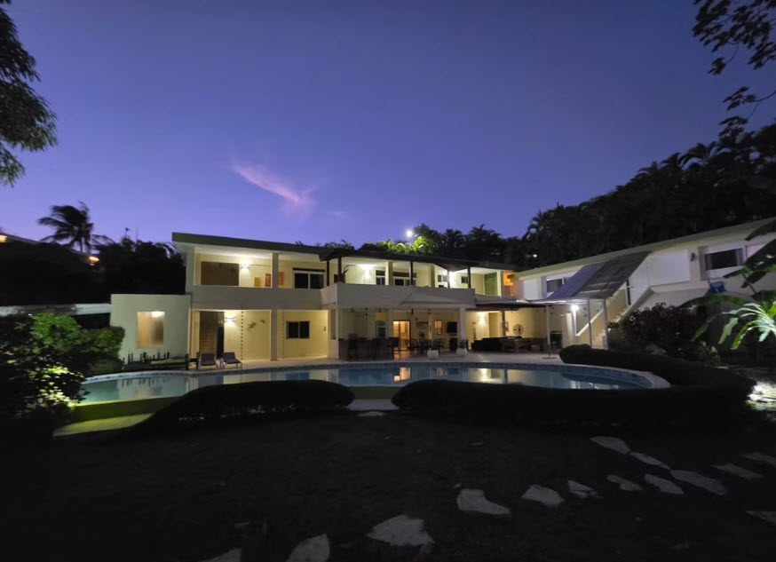 Luxury villa with pool at dusk, illuminated interior and tropical landscaping
