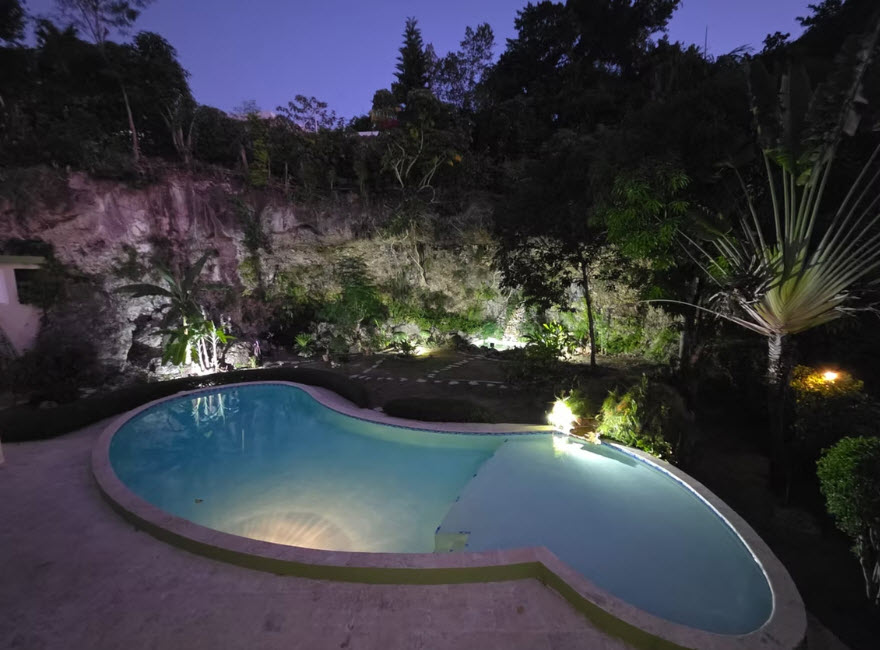 Illuminated tropical resort pool at dusk with lush landscaping.
