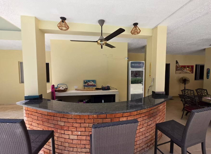 Curved brick bar with stools and Frigidaire cooler in outdoor seating area.