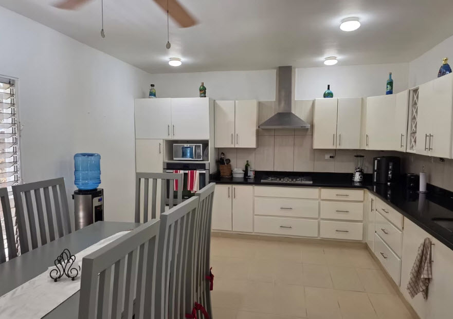 Modern white kitchen with dining table, stainless steel appliances, and granite countertops.