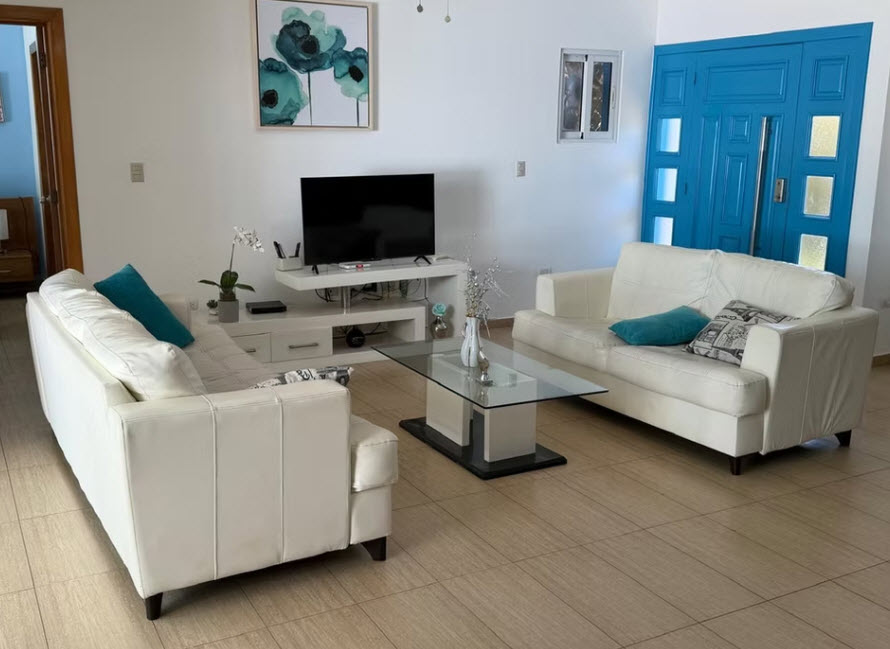 Modern living room with white leather sofas, glass coffee table, and bright blue door
