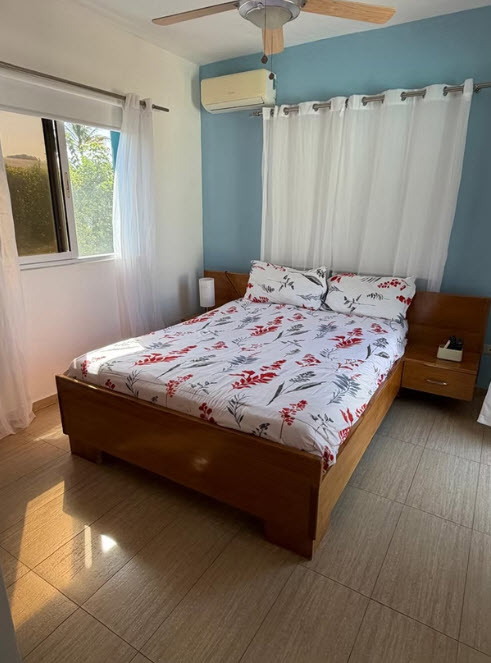 A cozy bedroom with a wooden bed, floral bedding, and a large window.