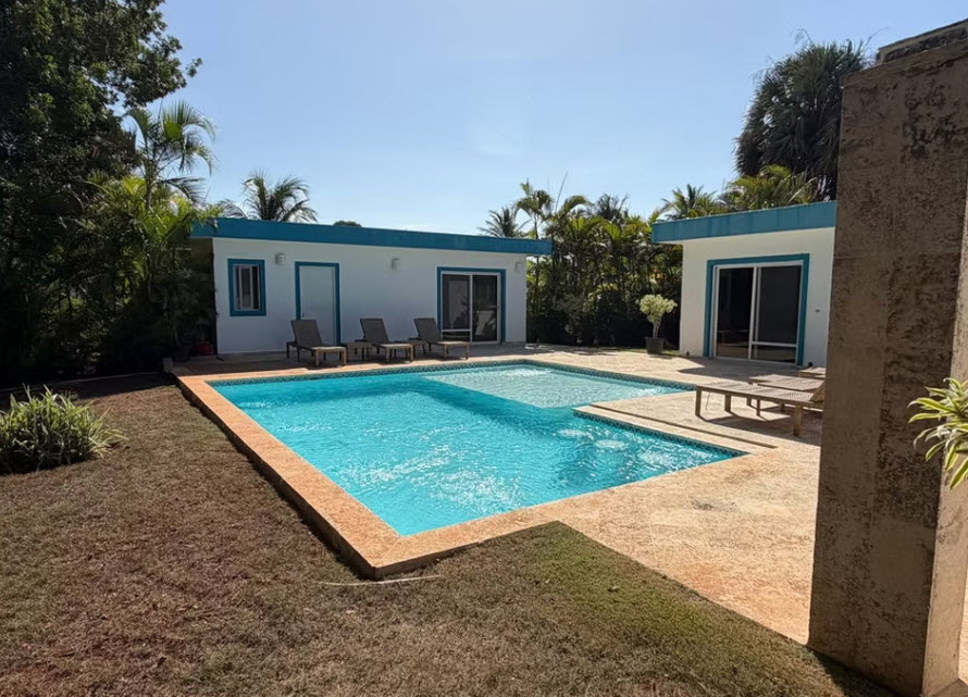 Modern villa with a rectangular swimming pool and lounge chairs in a tropical setting.