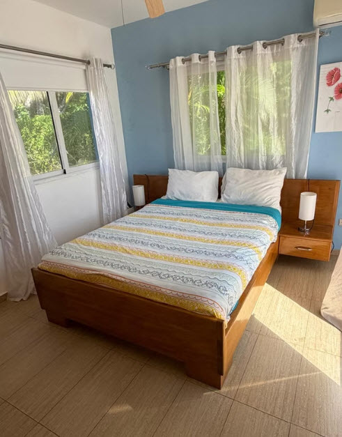 Cozy bedroom with a wooden bed, blue walls, and natural light from windows.