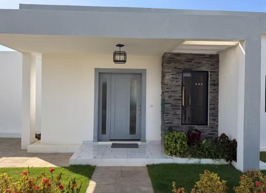 Modern grey front door of a white house with stone accents and garden
