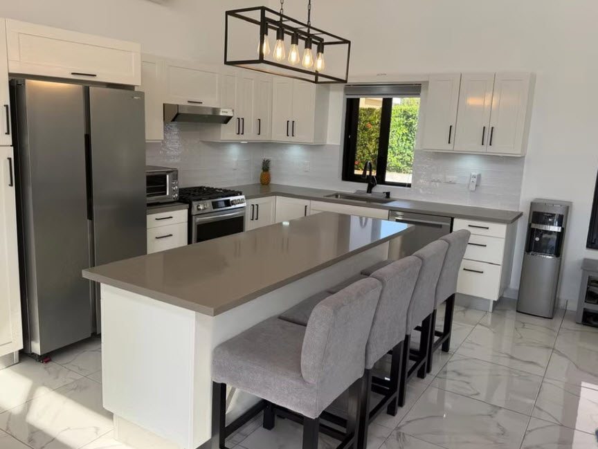Modern white kitchen with island, stainless steel appliances, and grey bar stools.
