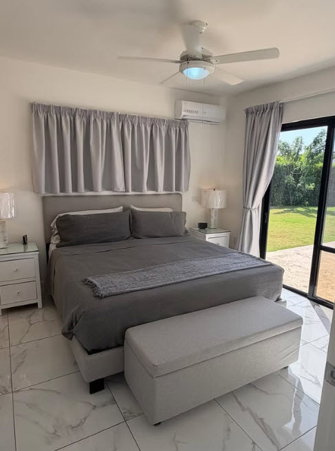Modern gray bedroom with king-size bed, bench, and large window overlooking garden