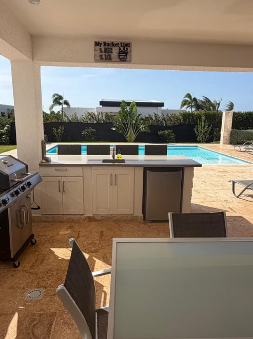 Outdoor kitchen with grill, sink, and mini-fridge next to a swimming pool.
