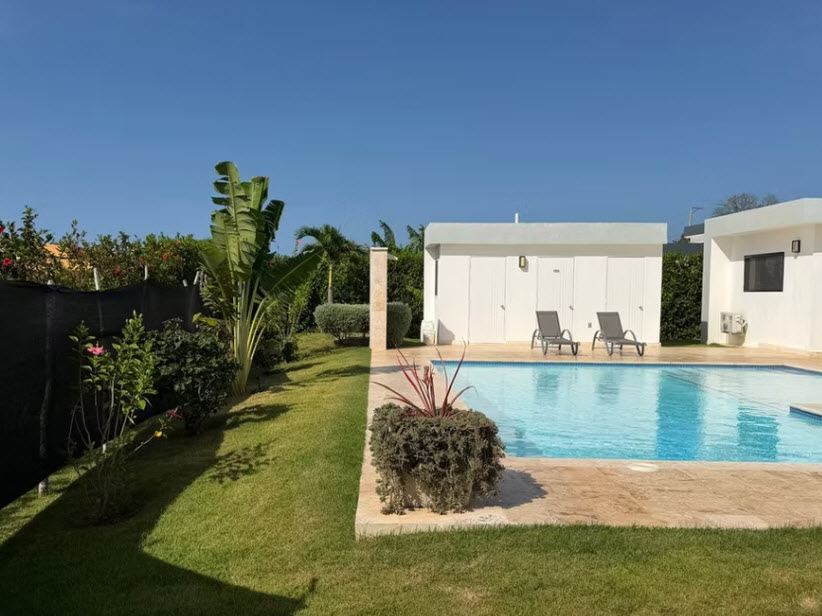 Sunny backyard with a swimming pool, lounge chairs, and lush landscaping.