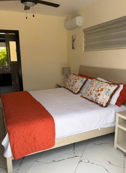 Cozy bedroom with a queen bed, orange throw, and floral pillows.