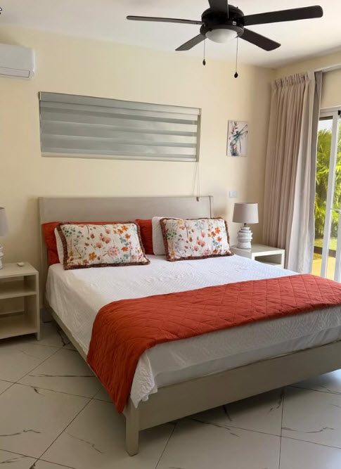 King-size bed with orange throw, floral pillows, and ceiling fan in a bright bedroom