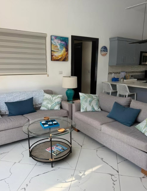 Modern living room with gray sofas, glass coffee table, and tropical decor