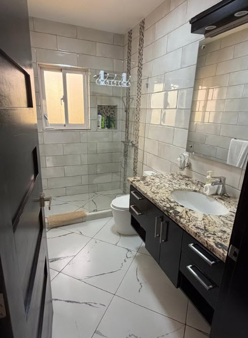 Modern bathroom with walk-in shower, granite vanity, and tiled walls.