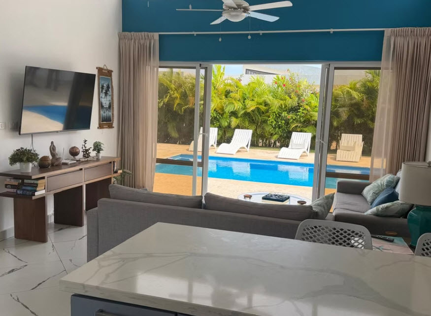 Modern living room with view of a blue swimming pool and tropical plants.