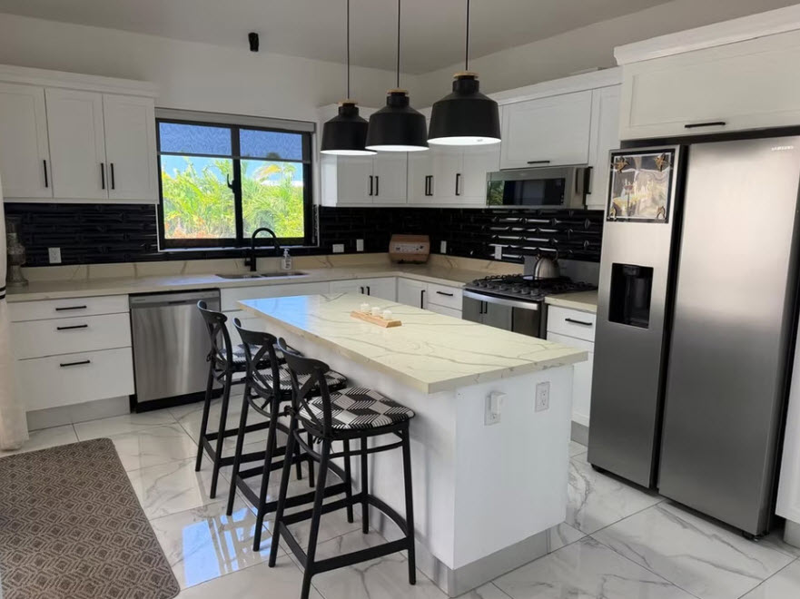 Modern white kitchen with island, black pendant lights, and stainless steel appliances