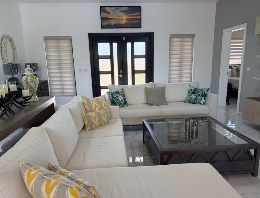 Modern living room with white sectional sofa, glass coffee table, and sunset art.