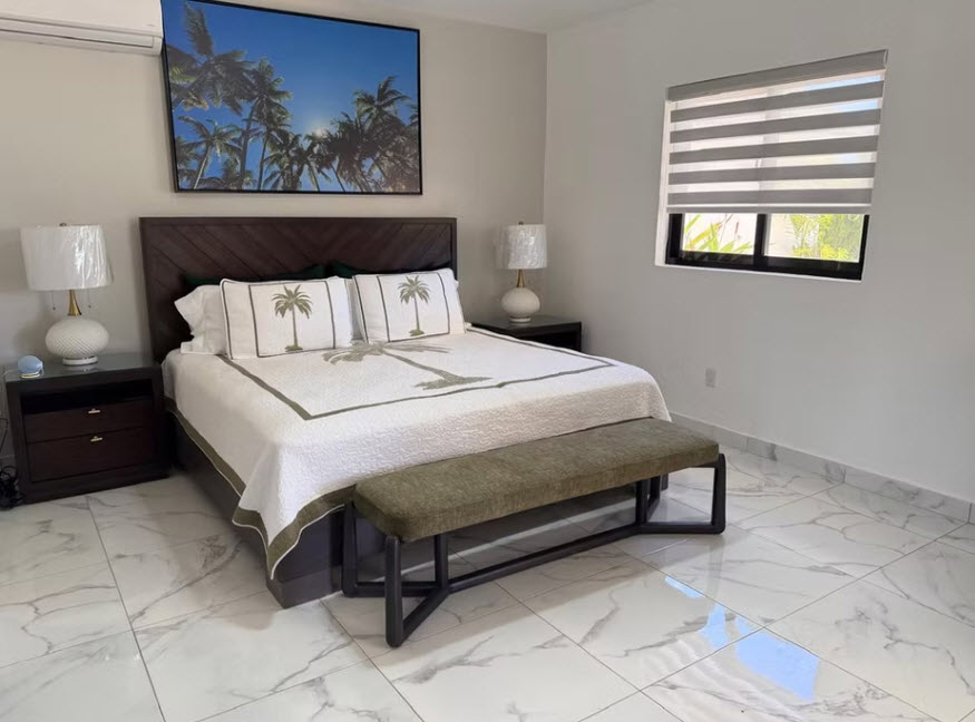 Tropical-themed bedroom with a king-size bed, palm tree artwork, and a bench