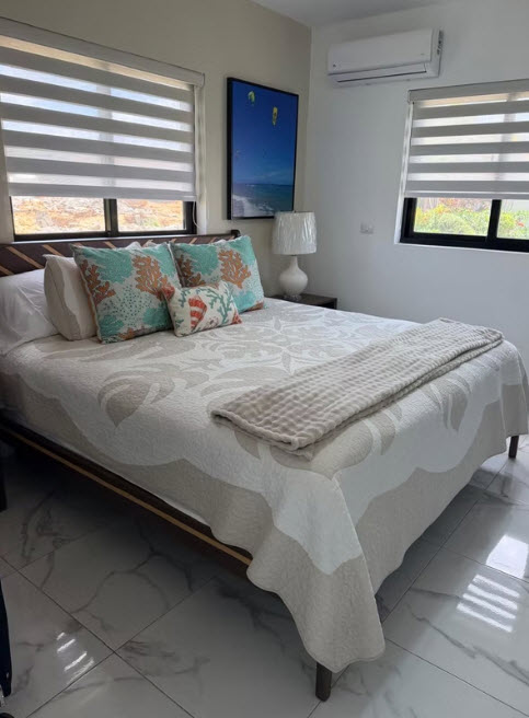 Modern bedroom with queen bed, coral-themed pillows, and ocean art