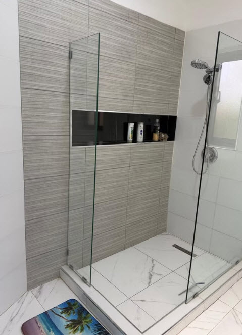 Modern walk-in shower with glass doors, tiled walls, and built-in shampoo niche.