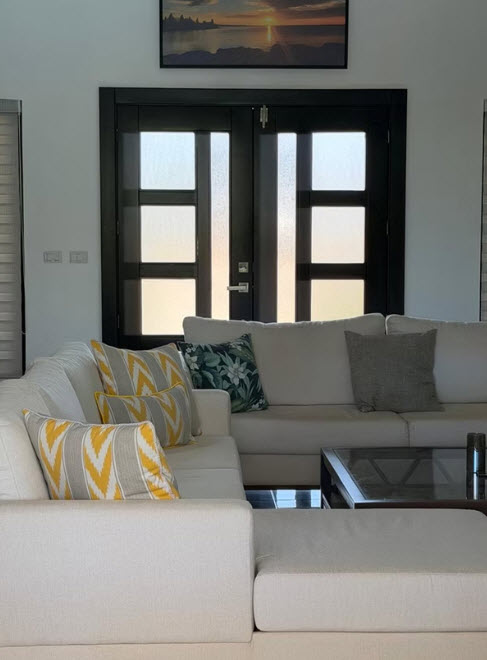Modern living room with white sectional sofa, patterned pillows, and dark double doors