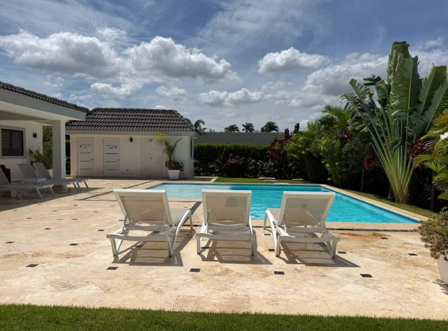 Luxury villa with swimming pool and lounge chairs in tropical setting.