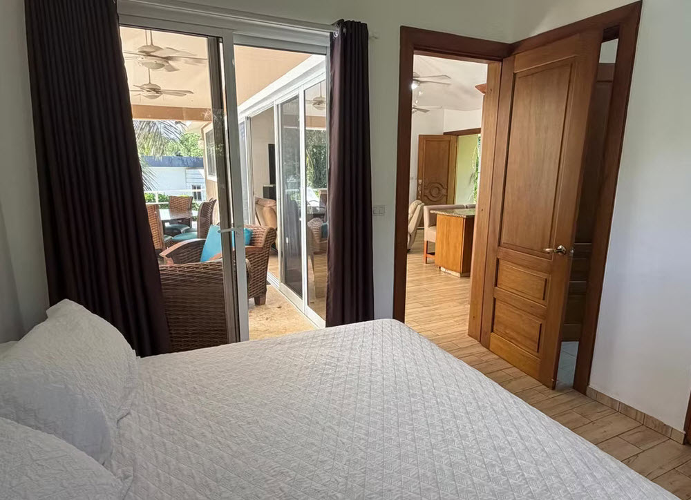 Bedroom with white comforter opens to a patio with wicker furniture.