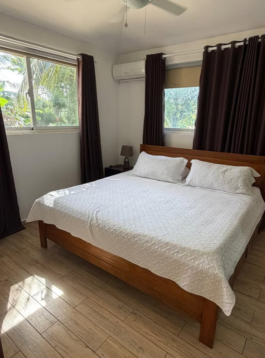 Sunlit bedroom with a wooden bed, white linens, and tropical views