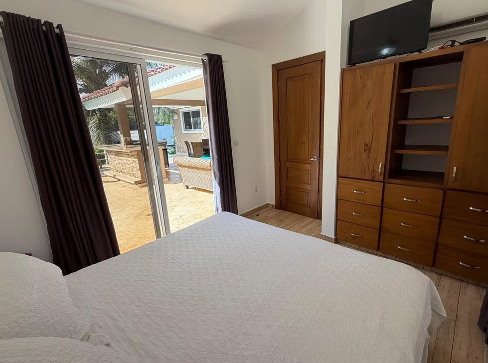 Bedroom with a large bed, wooden wardrobe, and sliding glass doors opening to an outdoor patio.