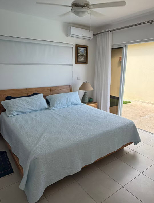 Bright bedroom with a queen-size bed, light blue bedding, and patio access.