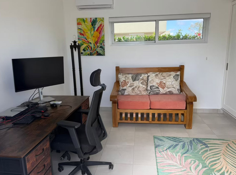 Modern home office with wooden desk, computer, chair, and tropical-themed artwork.