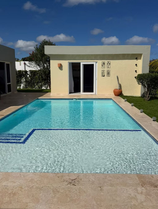 Modern backyard with a rectangular swimming pool and a light yellow building.