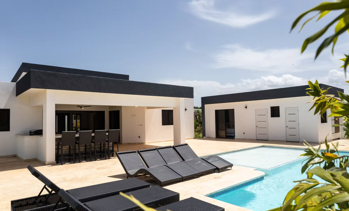 Modern villa with a swimming pool and lounge chairs under a blue sky.