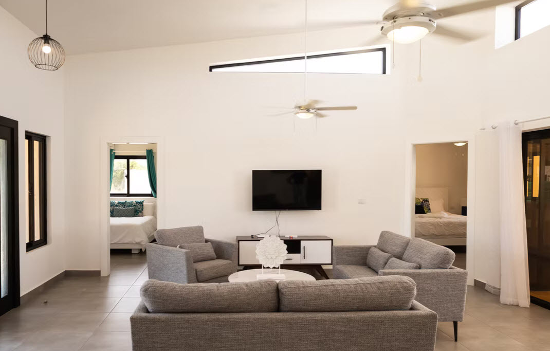 Modern living room with gray sofas, TV, and ceiling fans, open to bedrooms