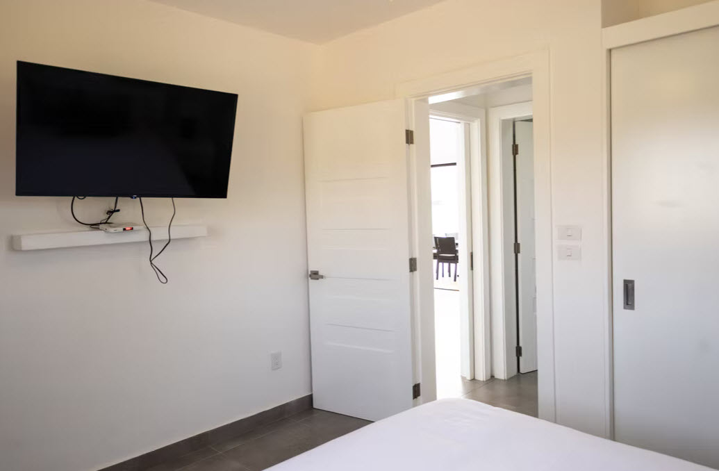 Modern bedroom with a wall-mounted TV and open doors revealing another room.