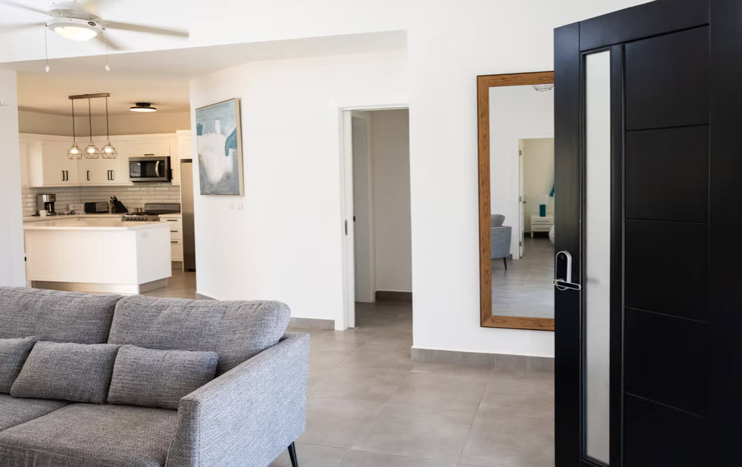 Modern living room with grey sofa, open kitchen, and large mirror reflecting hallway