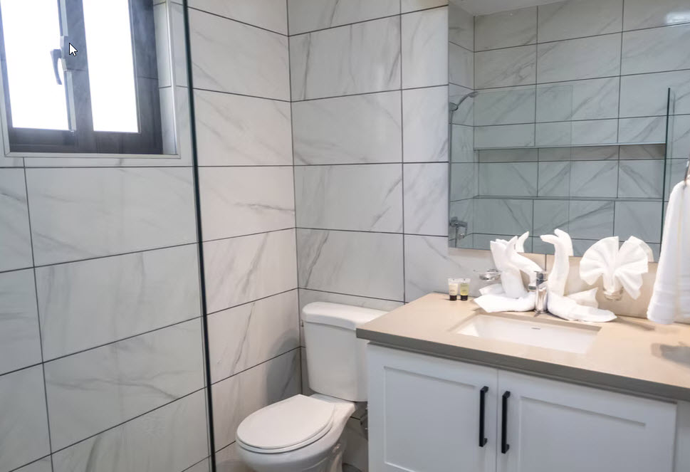 Modern bathroom with marble tiles, toilet, sink, and swan-shaped towels
