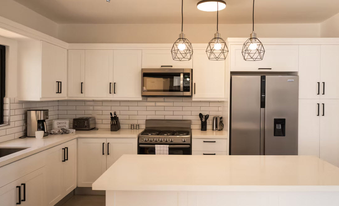 Modern white kitchen with stainless steel appliances and pendant lighting.