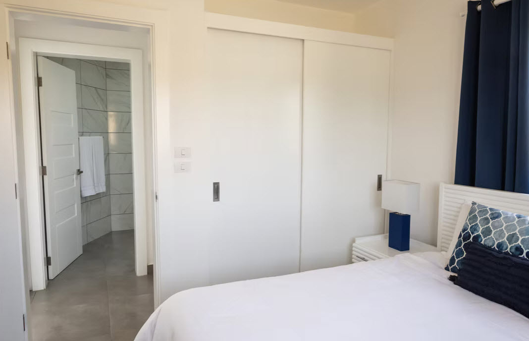 Modern bedroom with white sliding closet doors and a glimpse into a tiled bathroom