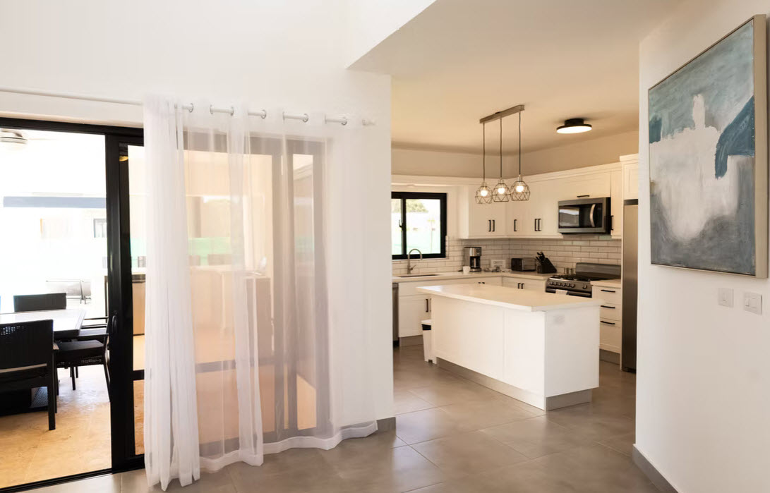 Modern white kitchen with island and dining area, bright natural light